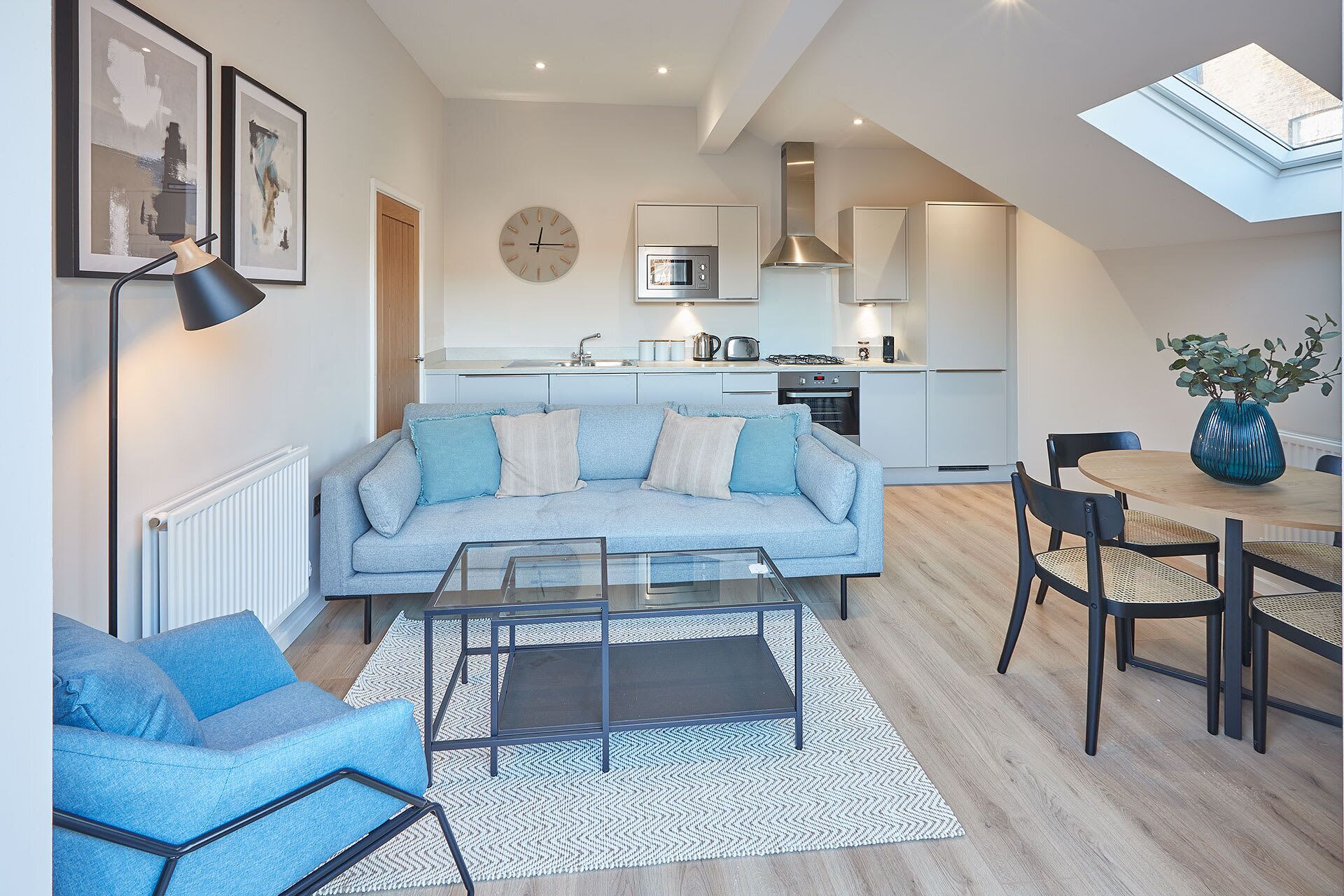 A modern living room with a sofa, coffee table, and chairs, a kitchen with appliances, and a dining area with a table and chairs.