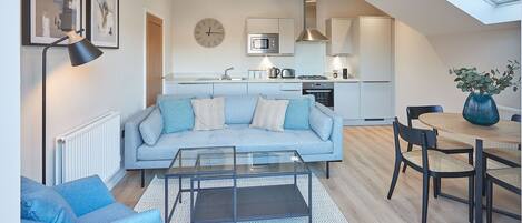 A modern living room with a sofa, coffee table, and chairs, a kitchen with appliances, and a dining area with a table and chairs.
