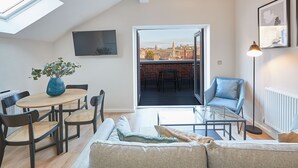 Ett modernt vardagsrum med en soffa, ett soffbord, en matplats med stolar, en tv och en balkong med utsikt över staden.
