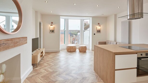 A modern kitchen with a herringbone floor pattern, wooden cabinetry, and a large island with a built-in oven. - Host Stay Abbey Hus (Whitby)