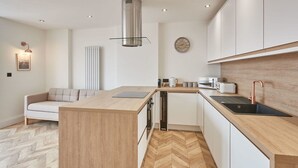 A modern kitchen with a central island, white cabinetry, and a herringbone wood floor. - Host Stay Abbey Hus (Whitby)