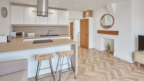 A modern kitchen with a central island, two bar stools, a herringbone-patterned floor, and a wooden door. - Host Stay Abbey Hus (Whitby)