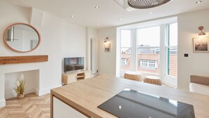 A modern kitchen with a built-in stove, wooden herringbone flooring, a round mirror, and a large window offering a view of the city. - Host Stay Abbey Hus (Whitby)
