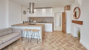A modern kitchen with a central island, white cabinetry, and a herringbone wood floor. - Host Stay Abbey Hus (Whitby)