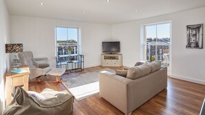 A spacious living room with a sofa, armchair, and ottoman, a TV on a stand, and a balcony with a view. - Host Stay Abbey Court Apartment (Whitby)