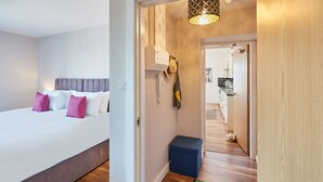 A modern hotel room with a bed, bedside table, and a small stool. There is a hallway leading to a kitchen area. - Host Stay Abbey Court Apartment (Whitby)