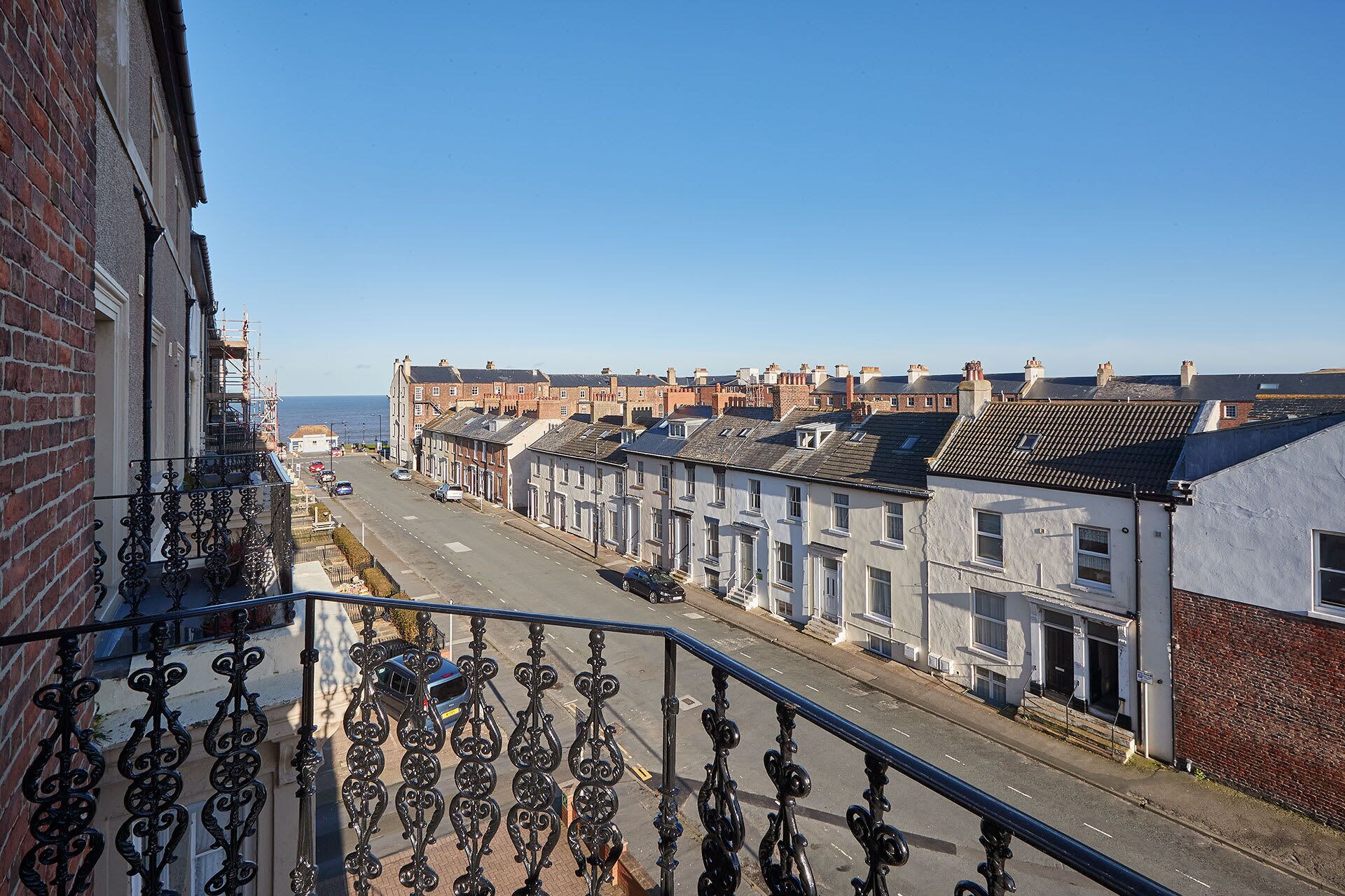 A residential street with terraced houses, a clear sky, and a view of the sea.