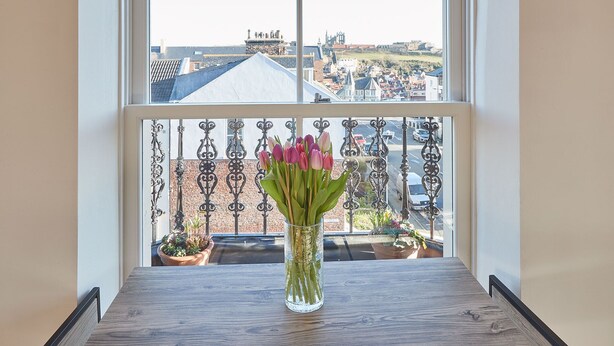 A balcony with a view of a cityscape, a vase with flowers, and a railing. - Host Stay Abbey Court Apartment (Whitby)