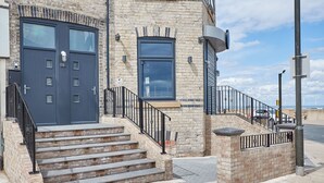 A two-story building with a dark blue front door, a staircase leading to the entrance, and a brick facade.