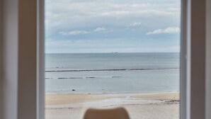 A view of a beach through a window, with a ship in the distance and a cloudy sky.