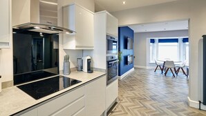 A modern kitchen with a black induction cooktop, stainless steel appliances, and a herringbone wood floor.