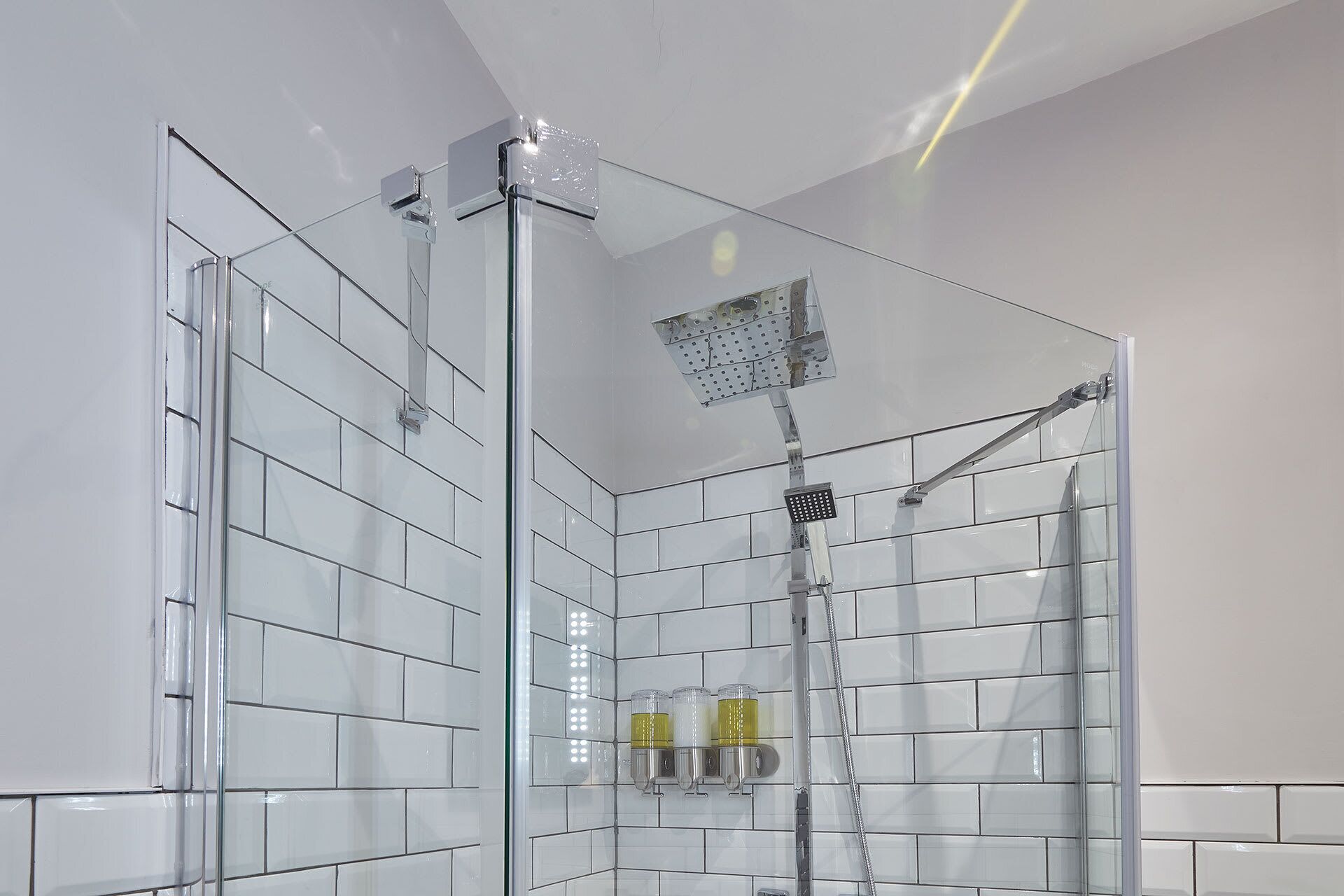 A glass-enclosed shower with a handheld showerhead and a wall-mounted faucet.
