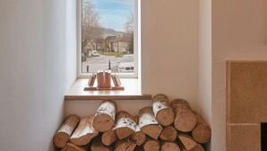 A window with a view of a street and houses, a wooden shelf with books, and a stack of logs. - Host Stay The Cobbles (Northallerton)