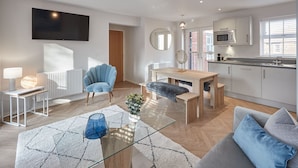 A modern living room with a sofa, a coffee table, a dining table, and a kitchen area with a microwave and sink.