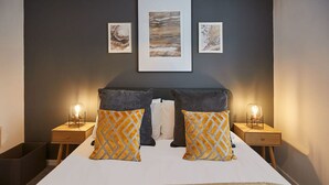 A bedroom with a large bed, two bedside tables with lamps, and three framed artworks on the wall.