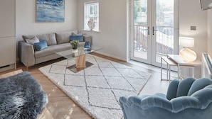 A modern living room with a sofa, a glass coffee table, a rug, and a view through a sliding glass door.