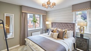 Une chambre à coucher avec un grand lit, une table de chevet, une lampe, une fenêtre avec des rideaux et un radiateur.