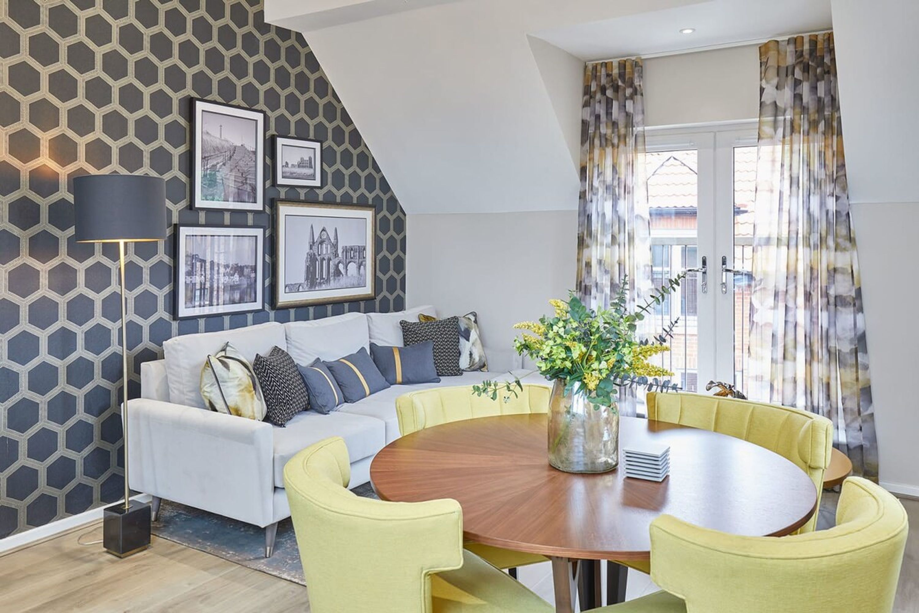 A modern living room with a white sofa, yellow chairs, a wooden dining table, and a cityscape wall.