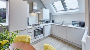 Une cuisine moderne avec des meubles blancs, une cuisinière à gaz, un four, une lucarne et un coin repas avec des chaises jaunes.