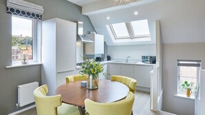 Une cuisine moderne dotée d’une verrière, un coin repas avec une table ronde et des chaises jaunes, et une vue sur la ville grâce à de grandes fenêtres.