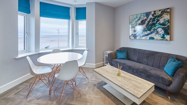 Un salon moderne avec un canapé gris, des chaises blanches, une table basse en bois et un grand tableau abstrait accroché au mur.
