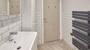 Une salle de bain avec un lavabo blanc, un miroir et une porte avec un revêtement en bois clair.