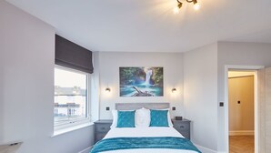Une chambre moderne avec un grand lit, une fenêtre donnant sur un beau paysage, un tableau représentant une cascade et une porte menant à une autre pièce.