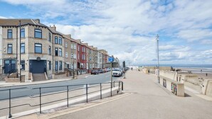 Une rue côtière bordée de maisons à étages, avec un chemin piétonnier et une plage en arrière-plan.