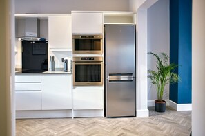 A modern kitchen with white cabinets, a stainless steel refrigerator, double ovens, and a potted plant. - Host Stay Bellevue Apartment 1 (Redcar)