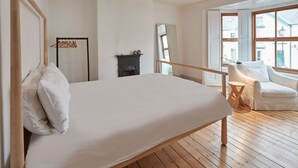Ein Schlafzimmer mit einem großen Bett, Holzboden, Kamin und einem Fenster mit Blick auf Gebäude.