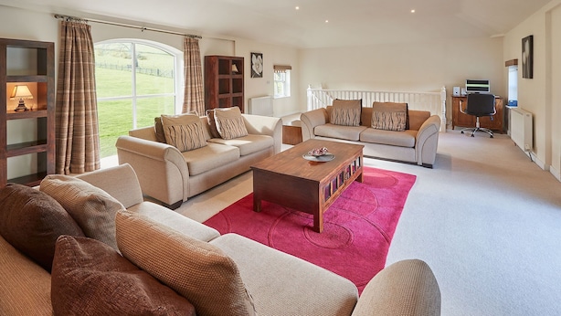 A spacious living room with a large sofa set, a coffee table, and a view of the outdoors through large windows. - Host Stay The Stable (Scarborough)