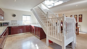 A spacious kitchen with a built-in island, a white staircase, and a dining area with a table and chairs. - Host Stay The Stable (Scarborough)
