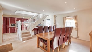 A spacious dining area with a wooden table and leather chairs, a staircase leading to a kitchen, and a large window with curtains. - Host Stay The Stable (Scarborough)