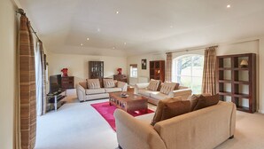 A spacious living room with a beige sofa, a coffee table, and a TV. There are wooden cabinets and a large window providing natural light. - Host Stay The Stable (Scarborough)