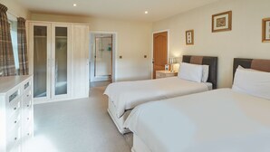 A hotel room with two beds, a wardrobe, a bathroom with a shower, and a bedside table with a lamp. - Host Stay The Stable (Scarborough)