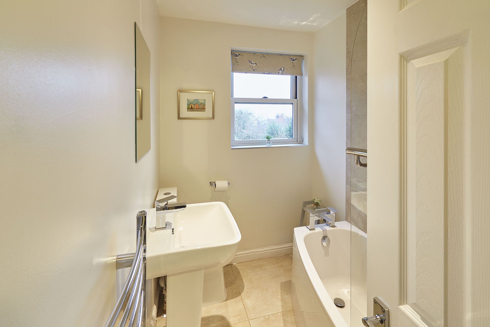 Et badeværelse med vask, toilet og badekar. Der er et vindue med udsigt til bygninger.