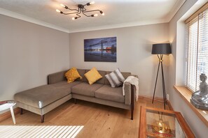 A living room with a sectional sofa, a floor lamp, a painting, and a statue.