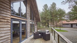A wooden deck with a table and chairs, a glass door entrance, and a view of trees. - Host Stay Simon Howe Lodge (Whitby)