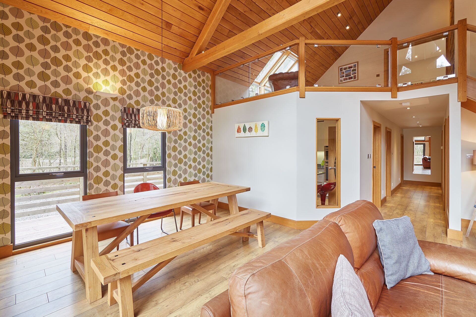 A spacious living area with a wooden dining table, leather sofa, and a view of the outdoors through large windows.