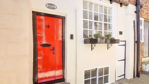 A red door with a number plate, a white window with multiple panes, and a small window with a mesh screen. - Host Stay Thimble Cottage (Whitby)
