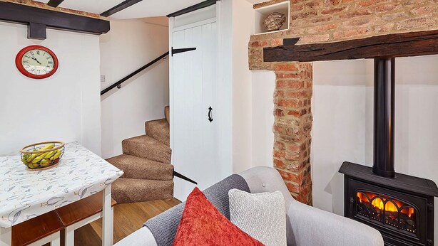 A cozy living room with a fireplace, a staircase, and a dining area with a table and chairs. - Host Stay Thimble Cottage (Whitby)