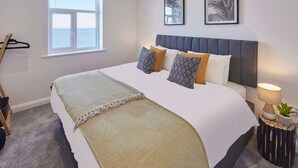 A bedroom with a bed, a window, a wall-mounted lamp, and two framed pictures. - Host Stay The Waves (Whitby)