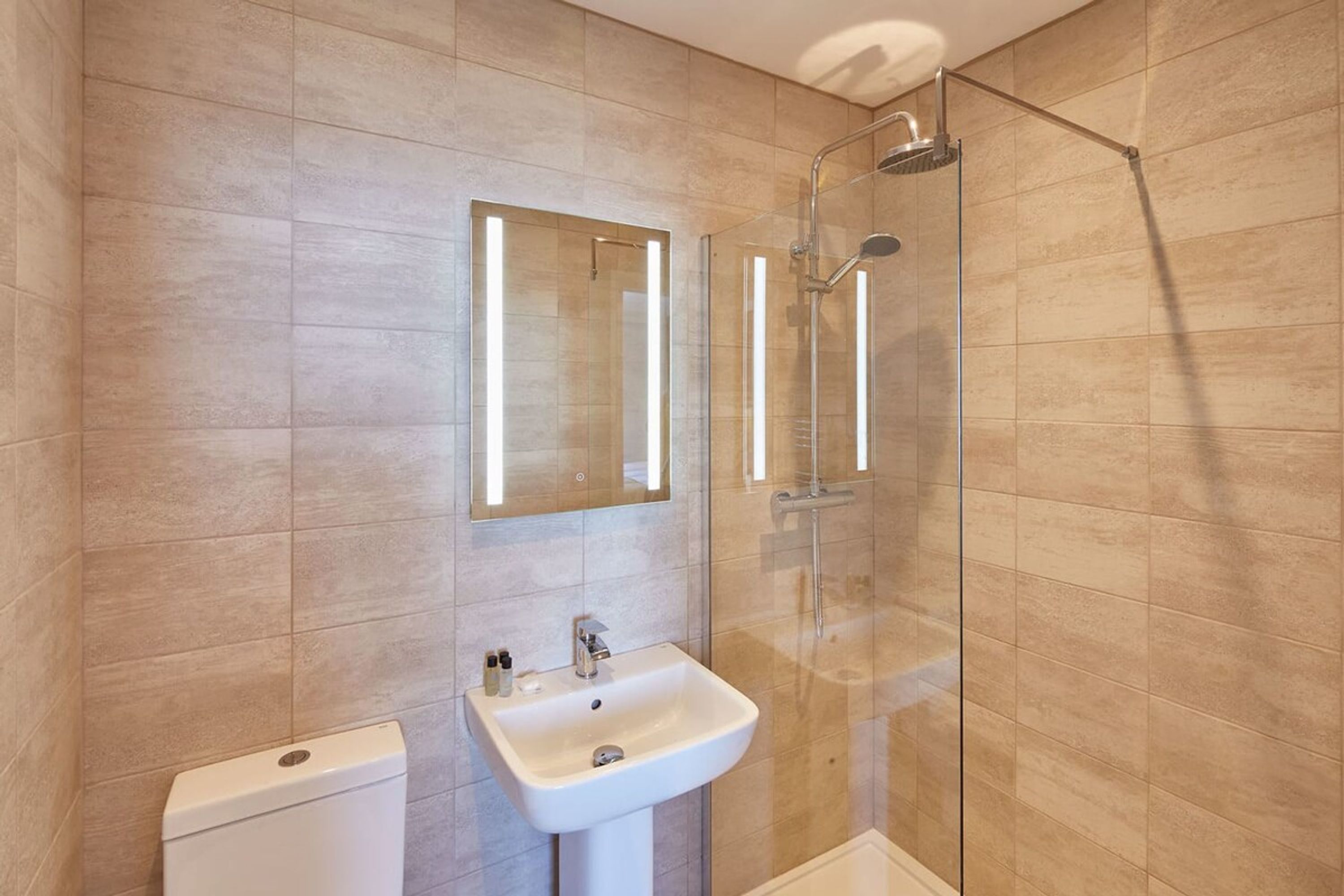 A modern bathroom with a glass-enclosed shower, a white pedestal sink, and a toilet.