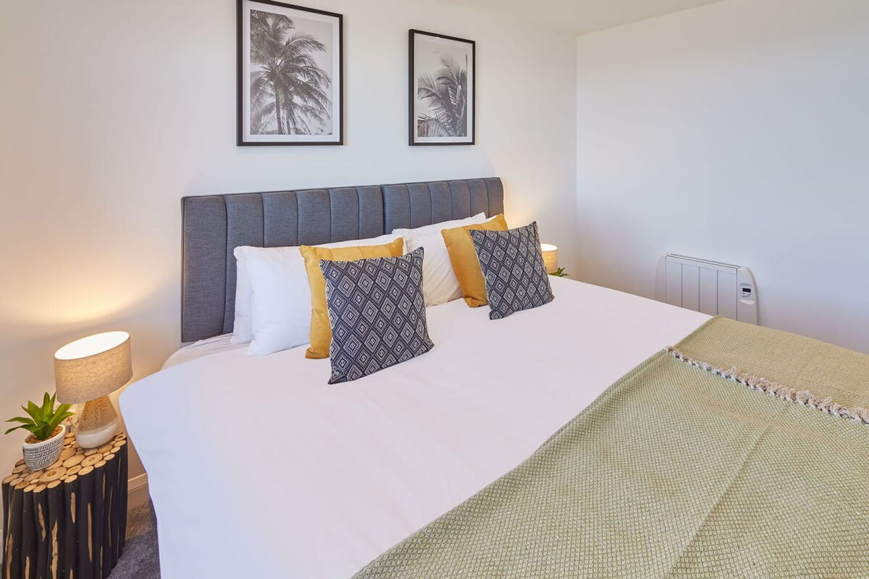 A neatly made bed with patterned pillows, a bedside lamp, and a small plant on a side table.