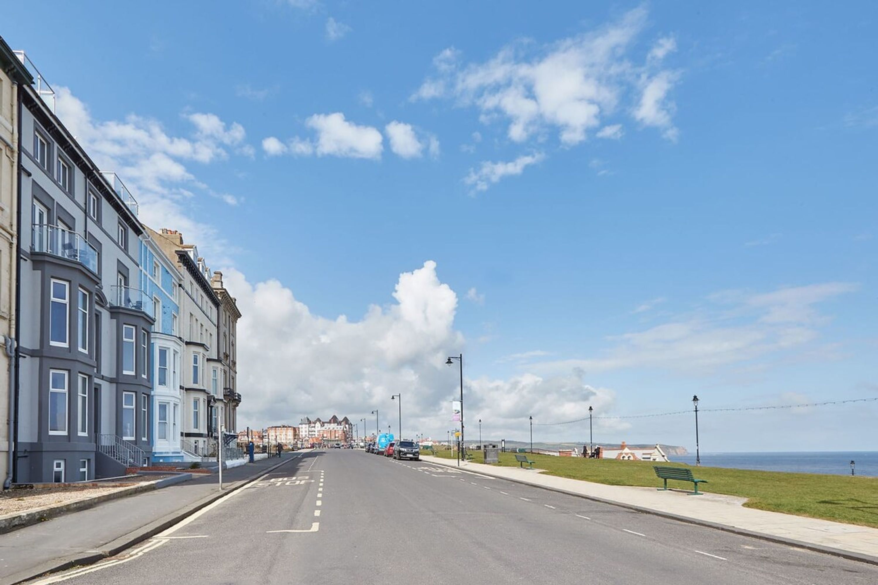 A coastal street with buildings on one side and a view of the sea on the other.