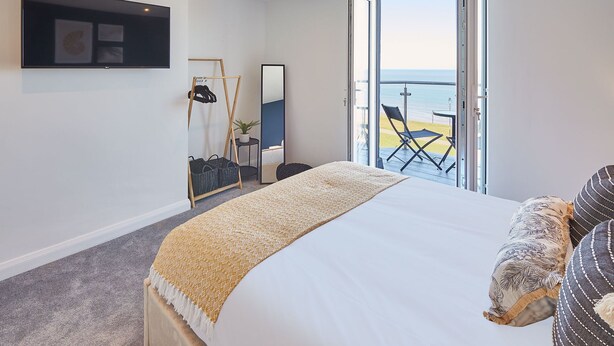 A hotel room with a bed, a seating area with a view of the sea, a balcony with a table and chairs, and a large window. - Host Stay The Waves (Whitby)