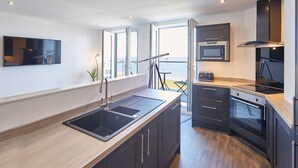 A modern kitchen with a large island, built-in oven, and a view of the sea. - Host Stay The Waves (Whitby)