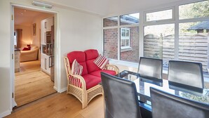 En hyggelig stue med en rød sofa, en fletstol og et spisebord med stole. Et køkken er synligt i baggrunden.