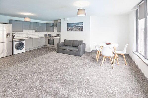 A modern kitchen with a washing machine, a dining area with a table and chairs, and a gray sofa. - Host Stay Apartment 2 Clarendon (Redcar)