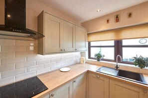 A modern kitchen with white cabinetry, a black stove, and a window with a view. - Host Stay Wood Street Cottage (Barnard Castle)